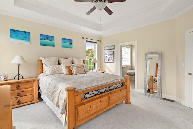 bedroom featuring a raised ceiling, ornamental molding, light colored carpet, ensuite bath, and baseboards