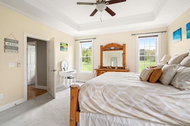 bedroom featuring light colored carpet, a tray ceiling, crown molding, baseboards, and ceiling fan
