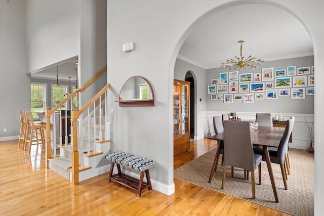 dining space featuring a chandelier, arched walkways, wood finished floors, ornamental molding, and stairs