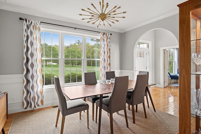 dining area with arched walkways, a chandelier, plenty of natural light, light wood-type flooring, and ornamental molding