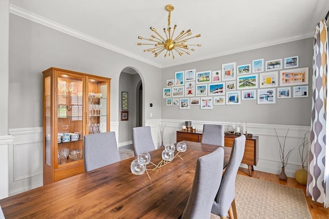 dining room with arched walkways, a chandelier, wood finished floors, ornamental molding, and a wainscoted wall