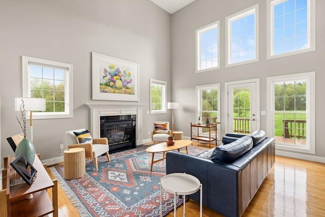 living room with a glass covered fireplace, plenty of natural light, light wood-type flooring, a high ceiling, and baseboards