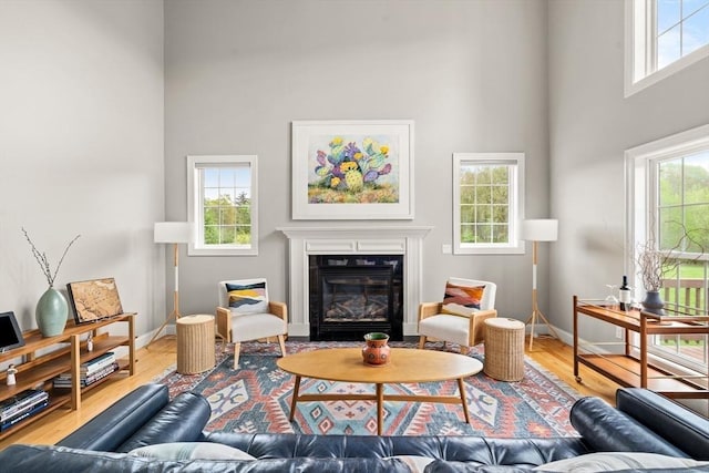 living room featuring a towering ceiling, healthy amount of natural light, baseboards, wood finished floors, and a fireplace with flush hearth