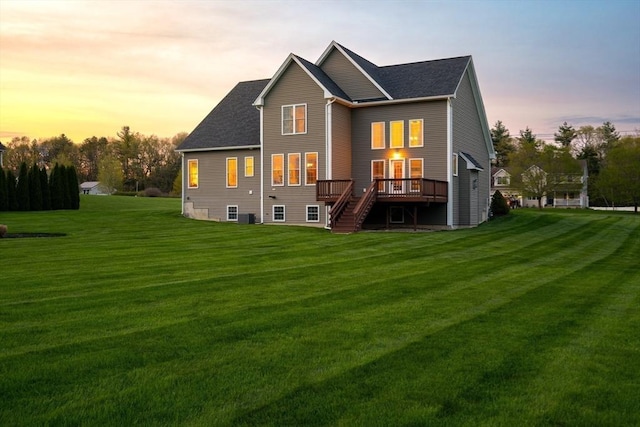 back of house at dusk with a wooden deck, stairs, a lawn, and a shingled roof