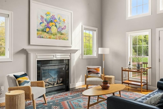 sitting room featuring healthy amount of natural light, a tiled fireplace, wood finished floors, and a towering ceiling