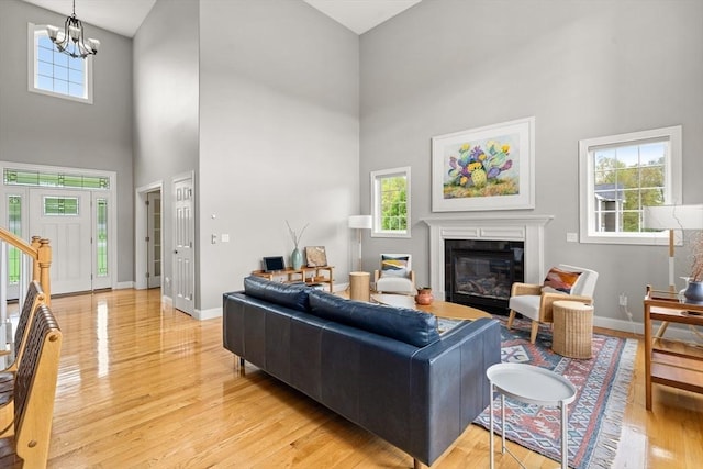 living room featuring a towering ceiling, light wood-style flooring, a glass covered fireplace, baseboards, and a chandelier