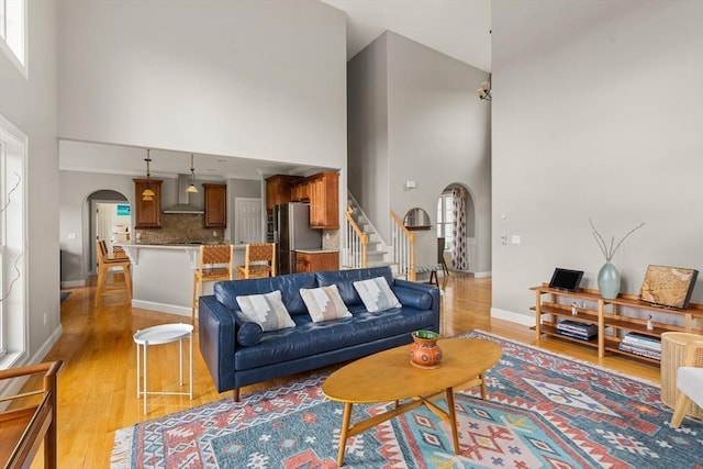 living room with arched walkways, a high ceiling, light wood-type flooring, stairway, and baseboards