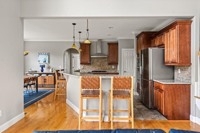 kitchen featuring wall chimney exhaust hood, stainless steel appliances, backsplash, a breakfast bar area, and crown molding
