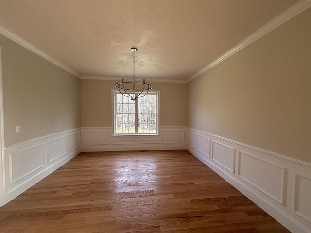 unfurnished dining area with hardwood / wood-style floors, ornamental molding, and a notable chandelier