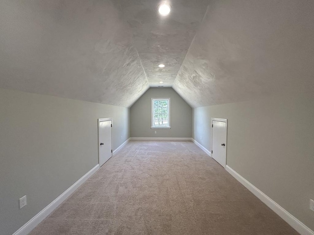 additional living space featuring vaulted ceiling, light colored carpet, and a textured ceiling