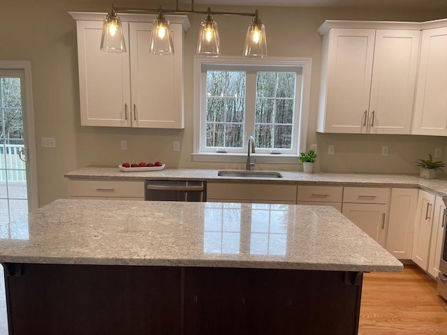 kitchen featuring light stone counters, stainless steel dishwasher, sink, decorative light fixtures, and white cabinetry