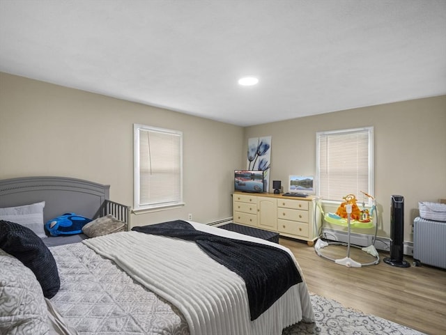 bedroom with multiple windows, light wood-type flooring, recessed lighting, and a baseboard heating unit
