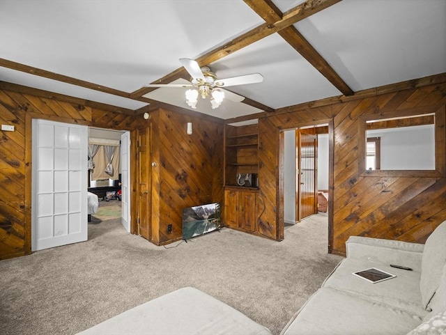 carpeted living room with wood walls, a ceiling fan, and beamed ceiling