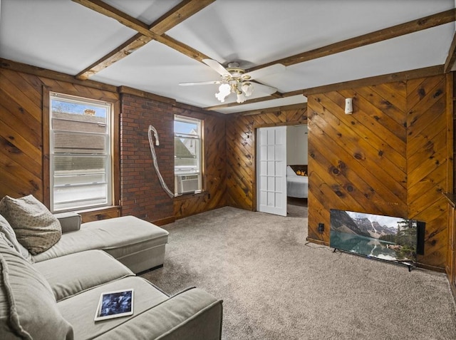 living area with wooden walls, carpet, ceiling fan, and beam ceiling