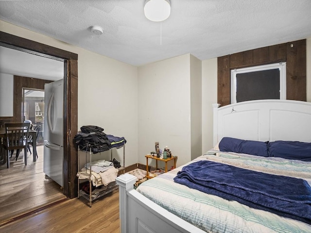 bedroom with freestanding refrigerator, light wood-style flooring, and a textured ceiling