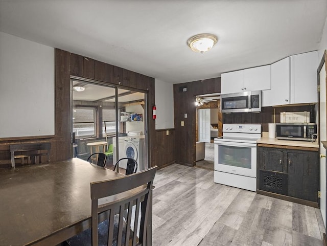 kitchen with white electric range, stainless steel microwave, washer / dryer, wood walls, and white cabinetry