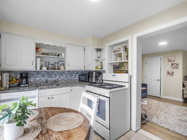 kitchen with open shelves, gas range gas stove, a sink, white cabinetry, and dark stone counters