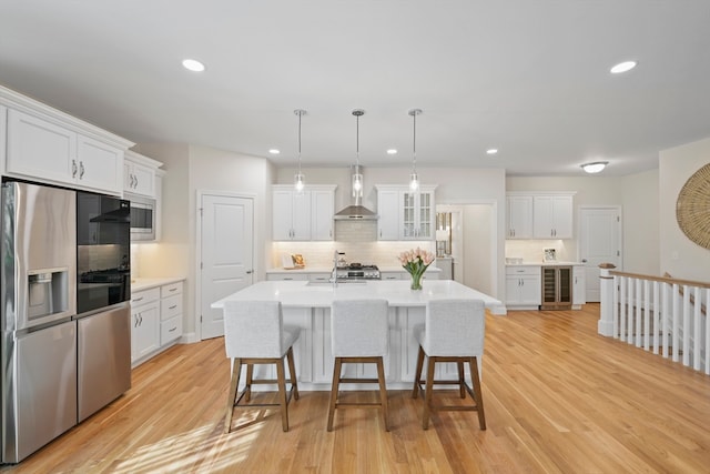 kitchen featuring white cabinets, wall chimney exhaust hood, stainless steel appliances, and light hardwood / wood-style floors