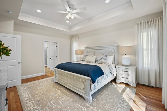 bedroom with ceiling fan, a raised ceiling, light wood-type flooring, and ornamental molding