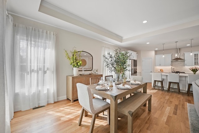 dining space with a raised ceiling, crown molding, and light wood-type flooring