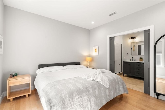 bedroom featuring a sink, light wood-type flooring, recessed lighting, baseboards, and ensuite bath