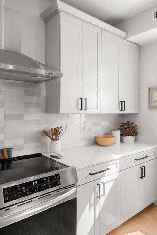kitchen with electric stove, wall chimney range hood, and white cabinetry