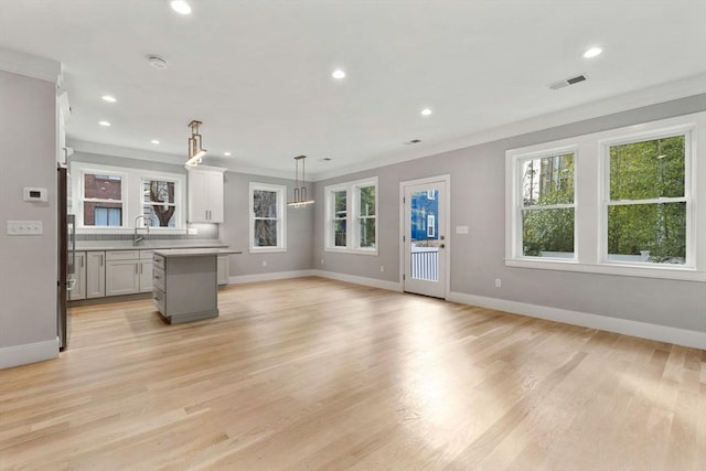 unfurnished living room with sink, light wood-type flooring, and ornamental molding