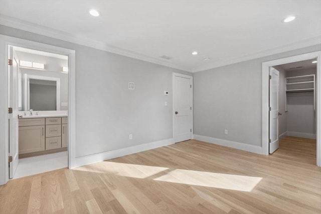 unfurnished bedroom featuring ensuite bathroom, a walk in closet, ornamental molding, light hardwood / wood-style floors, and a closet