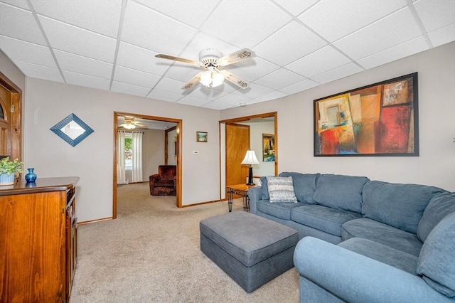 living area with a paneled ceiling, a ceiling fan, light carpet, and baseboards