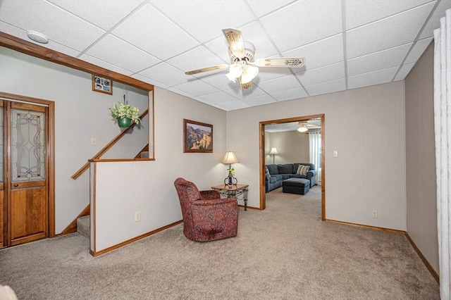 sitting room with a ceiling fan, carpet floors, a paneled ceiling, stairway, and baseboards