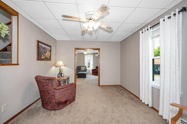 living area featuring a ceiling fan, a drop ceiling, carpet flooring, and baseboards