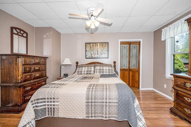 bedroom with wood finished floors, a paneled ceiling, baseboards, and ceiling fan