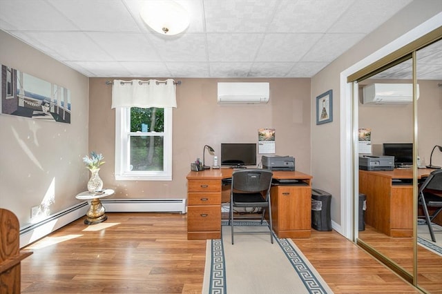 home office featuring light wood-type flooring, a wall unit AC, a paneled ceiling, and a baseboard heating unit