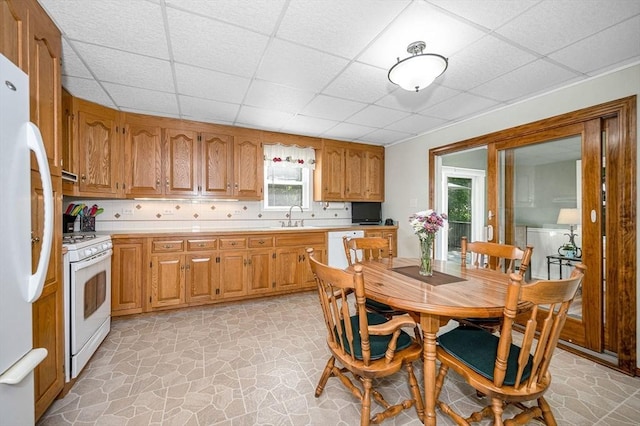kitchen with white appliances, a sink, a drop ceiling, light countertops, and stone flooring