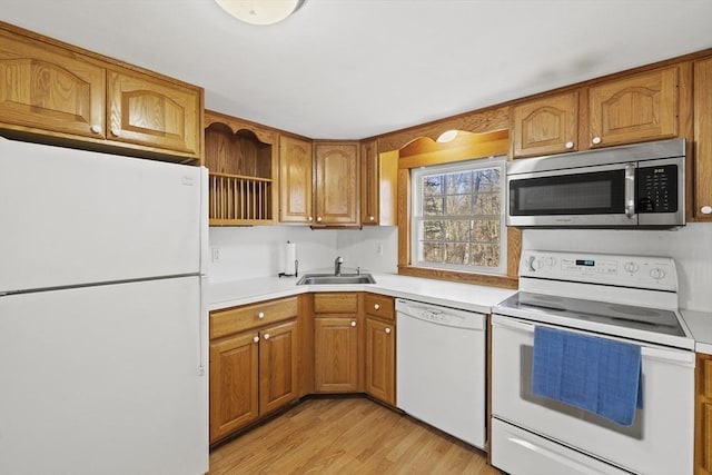 kitchen with white appliances, light countertops, a sink, and brown cabinetry