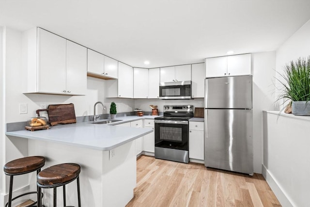1 Archer St, Swampscott, MA 01907 - kitchen with stainless steel appliances, a peninsula, light wood-style flooring, white cabinetry, and a kitchen bar