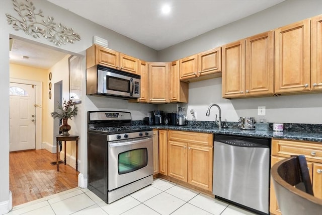 kitchen with stainless steel appliances, sink, light tile patterned floors, and dark stone counters