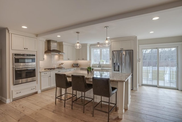 41 Pleasant St, Holliston, MA 01746 - kitchen with wall chimney range hood, stainless steel appliances, light wood-style floors, a center island, and light stone counters