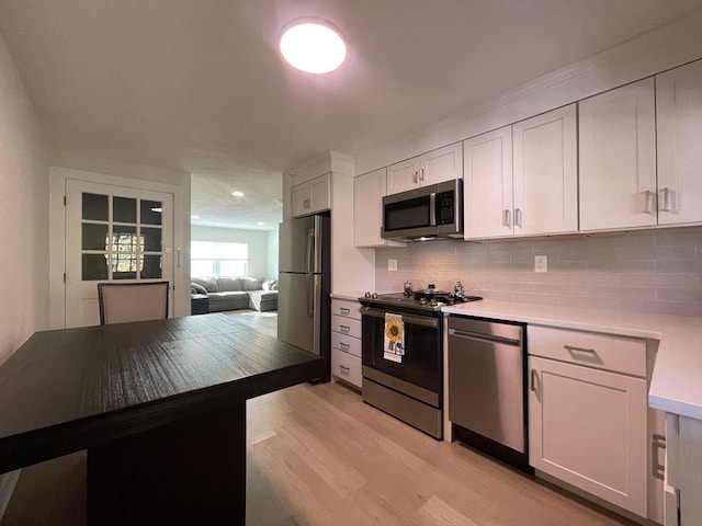 kitchen featuring tasteful backsplash, light wood-type flooring, white cabinets, and appliances with stainless steel finishes