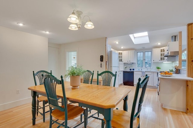 dining area with an inviting chandelier, light wood-type flooring, and a skylight