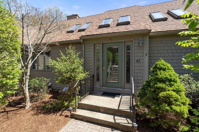 view of exterior entry with a shingled roof and a chimney