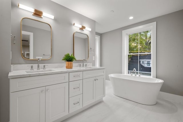 full bath with double vanity, marble finish floor, recessed lighting, a freestanding bath, and a sink