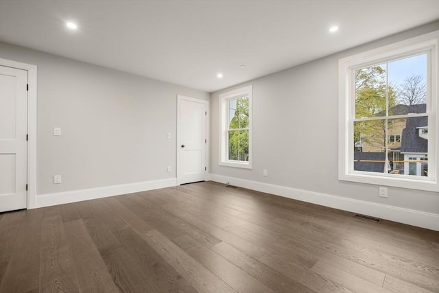 spare room with visible vents, baseboards, dark wood-type flooring, and a healthy amount of sunlight