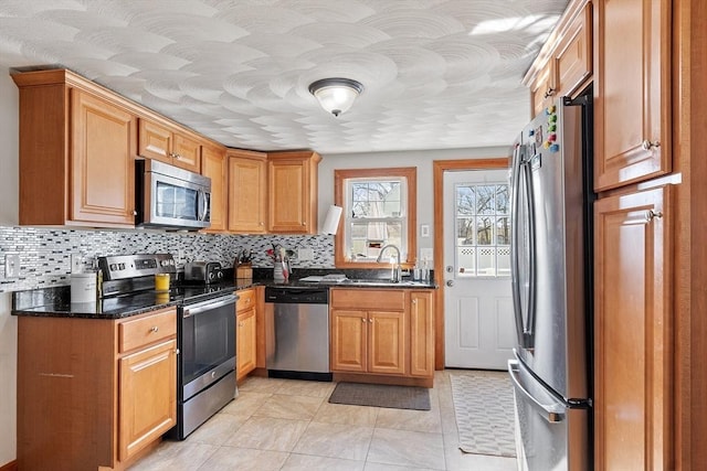 kitchen featuring dark stone counters, light tile patterned floors, appliances with stainless steel finishes, backsplash, and a sink