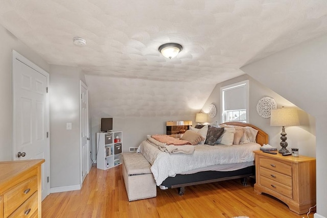 bedroom featuring a textured ceiling, light wood-type flooring, vaulted ceiling, and baseboards
