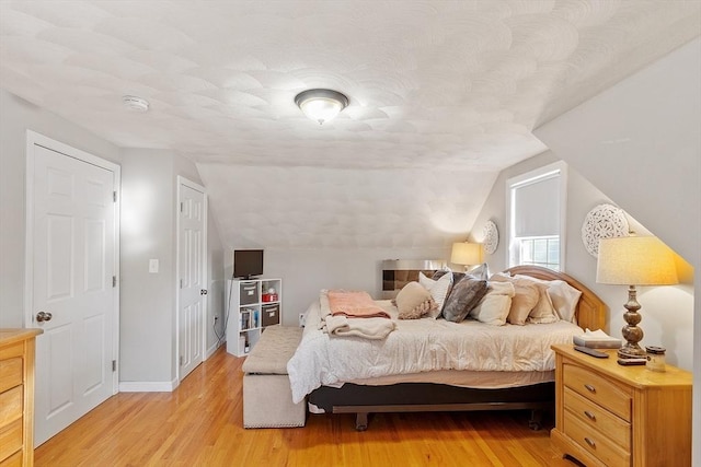 bedroom with baseboards, light wood-type flooring, and vaulted ceiling