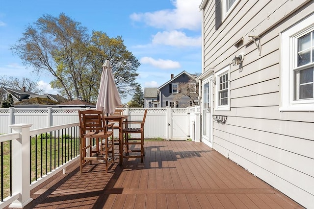 wooden terrace with outdoor dining area, a fenced backyard, and a gate