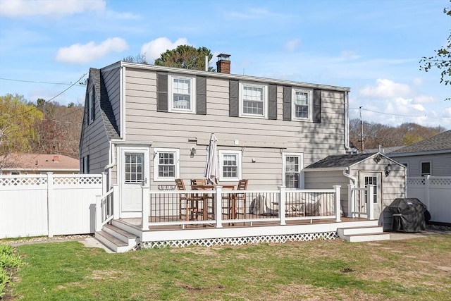 rear view of house with a chimney, fence, a wooden deck, and a lawn
