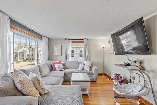 living room featuring a textured ceiling, baseboards, and light wood-style floors