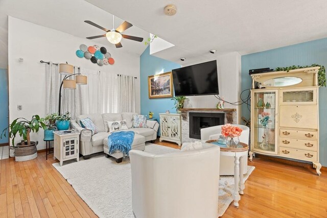 living area with a fireplace, lofted ceiling, hardwood / wood-style flooring, and a ceiling fan